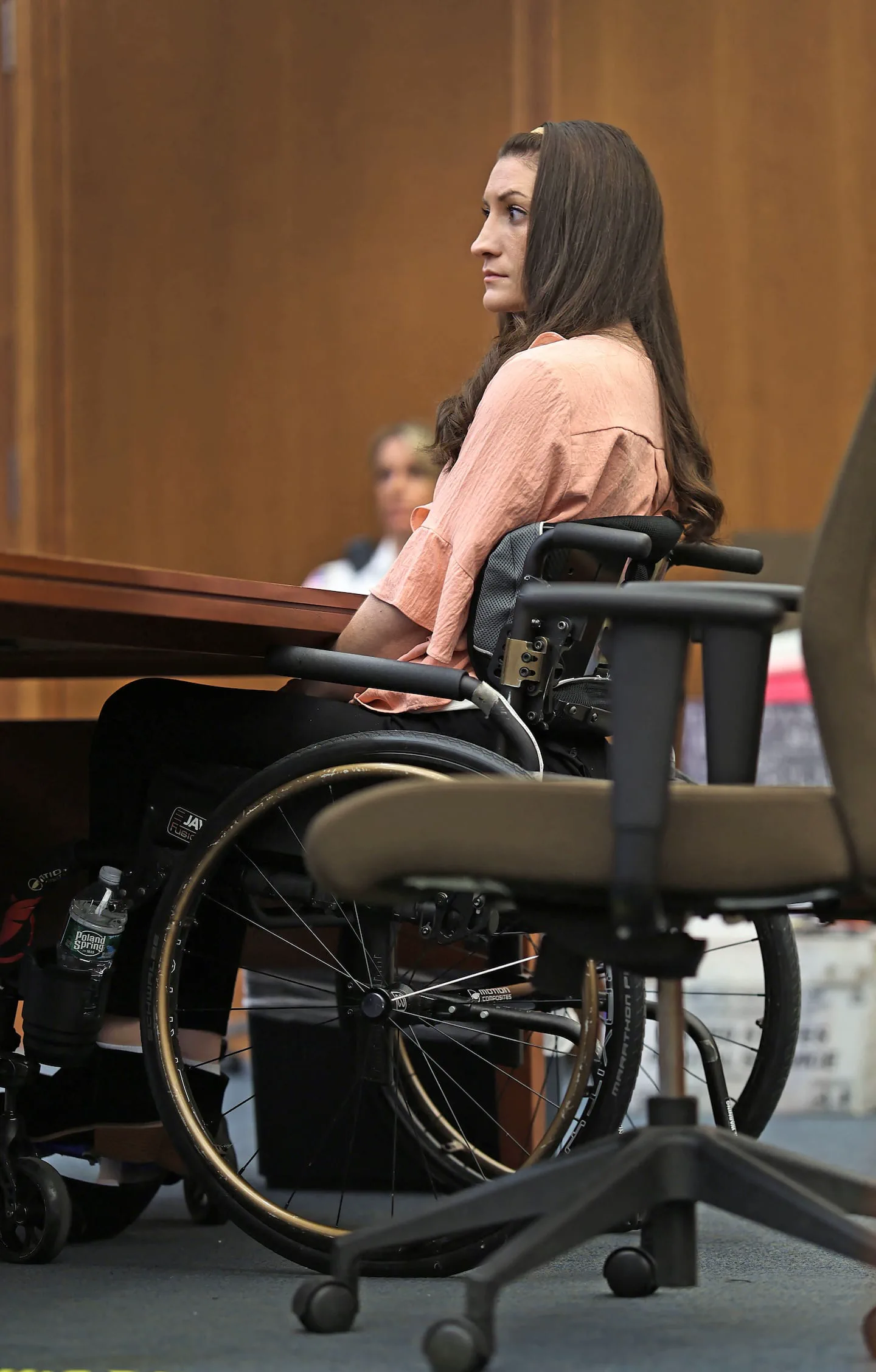 Una mujer de perfil sentada en silla de ruedas junto a una mesa de madera.